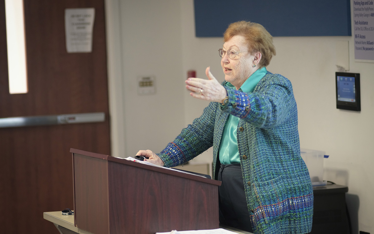 Liz Shelton gestures while delivering a lecture from a podium at American University.